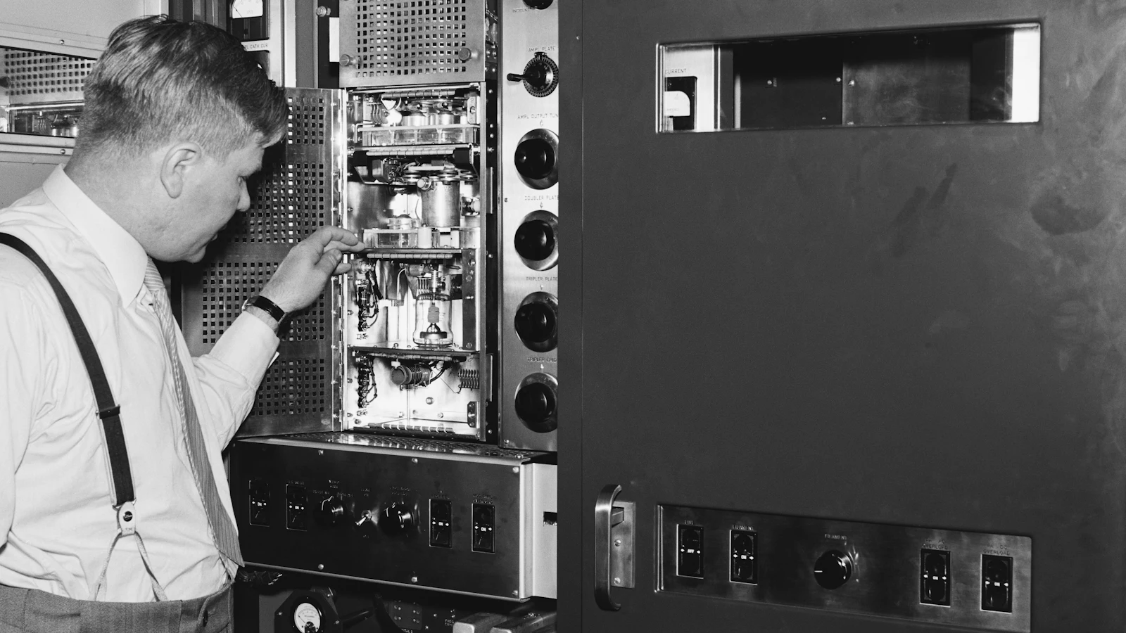 An archive photograph of a man working inside a rack of valve equipment: a person and a machine doing one job between them, which is the comparison this post makes