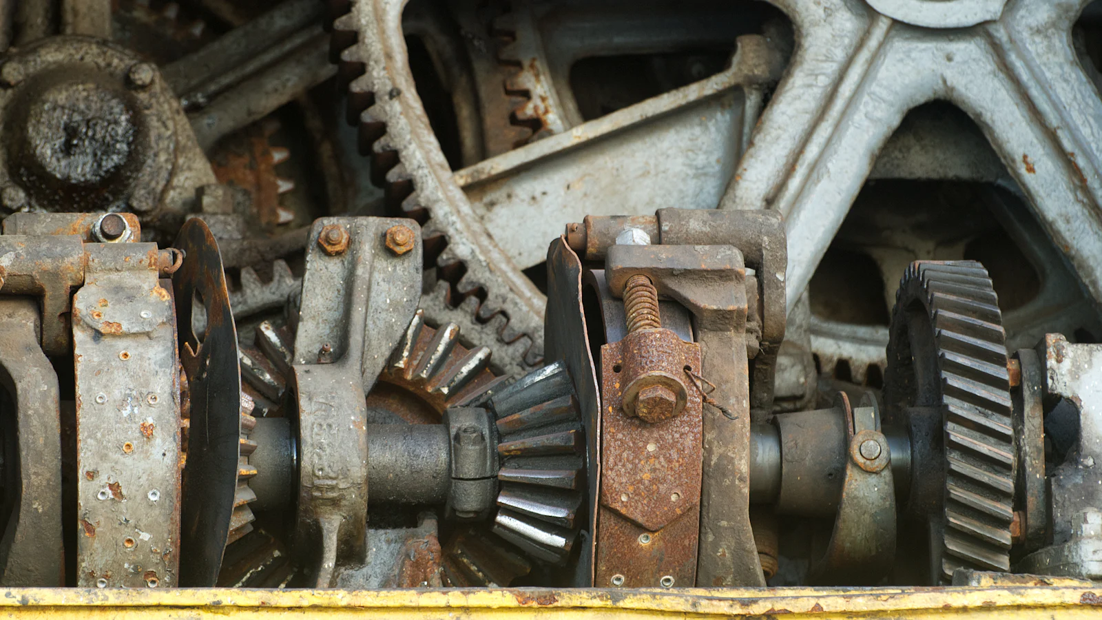 A dense mesh of rusted gears, bevel pinions, shafts and levers on old machinery, where nothing turns on its own and the order everything moves in is fixed by what it meshes with