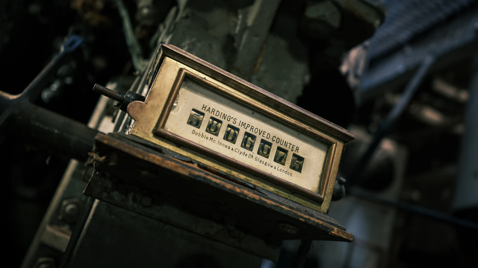 A brass mechanical counter bolted to workshop machinery, digit wheels showing a running tally — a number that only means anything once it is written down and compared with the next one