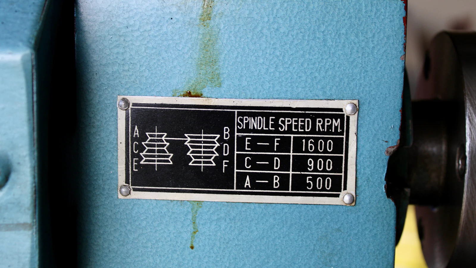 A riveted instruction plate on a machine, headed SPINDLE SPEED R.P.M., carrying a pulley diagram and a table of three exact figures rather than a description of how fast to run