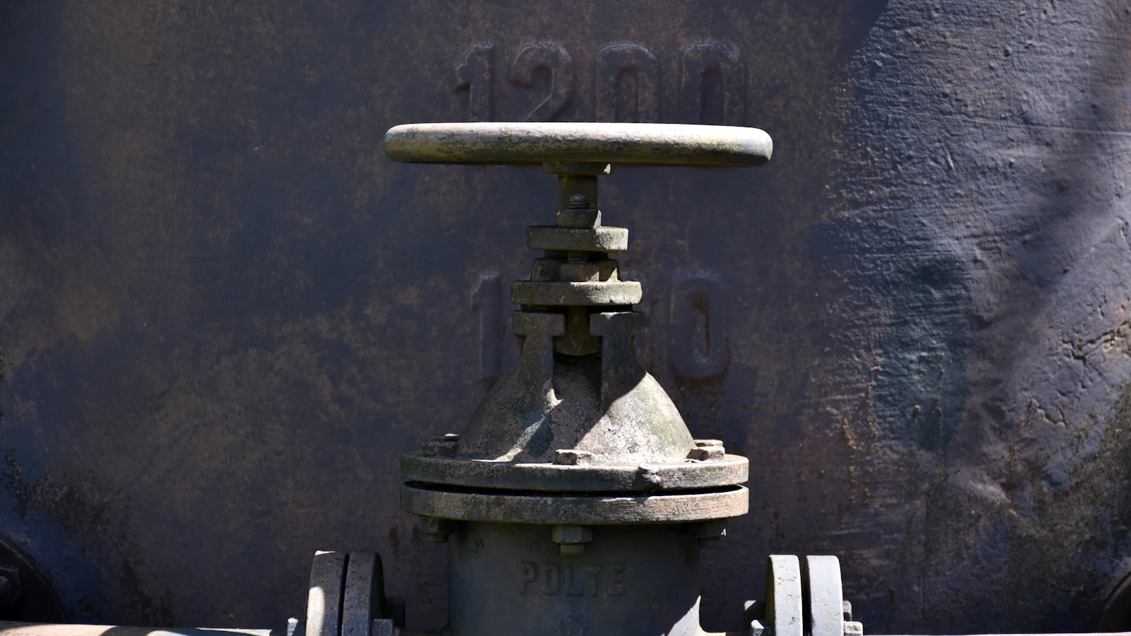 A weathered cast-iron gate valve and its handwheel against a plate cast with 1200, a gate nobody has turned in years and whose seal is assumed rather than tested