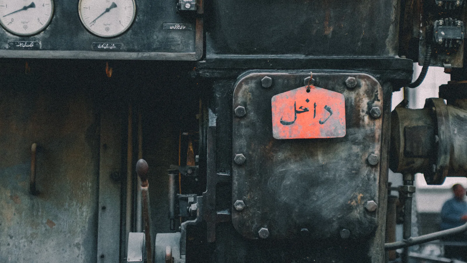 Pressure gauges and a worn red warning plate on a dark industrial machine — the readings you check to find out what is wrong while everything still looks fine